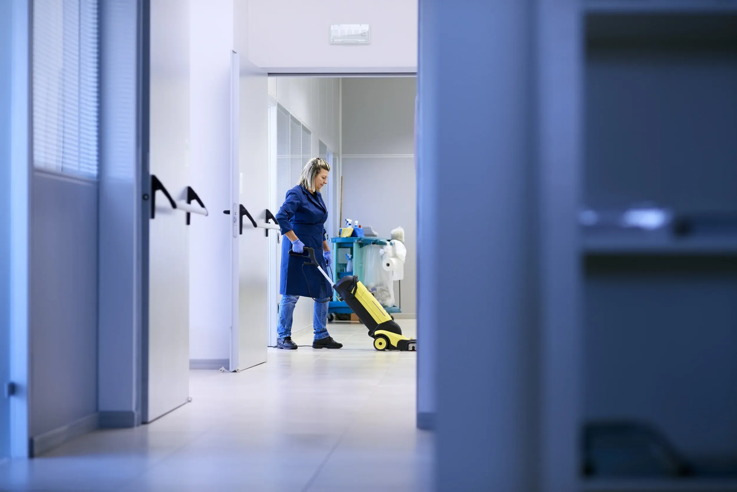 Cleaner running a floor machine in an office hallway